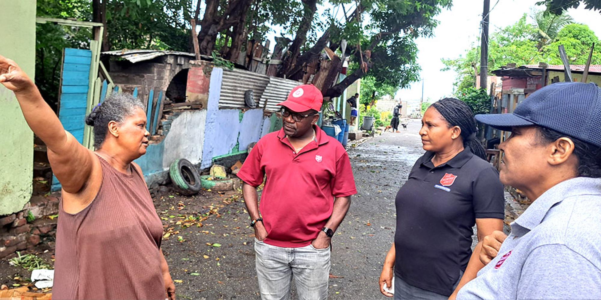 Three Salvation Army workers speak to a woman, hurricane devastation in the background